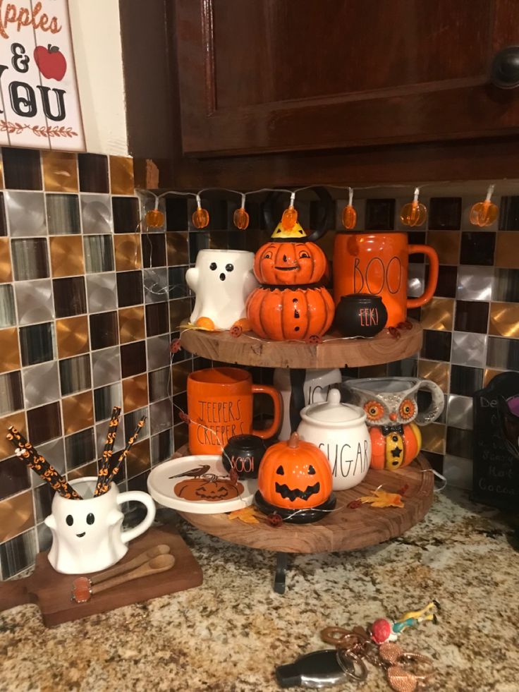 two tiered trays filled with coffee mugs and halloween themed decorations on a kitchen counter