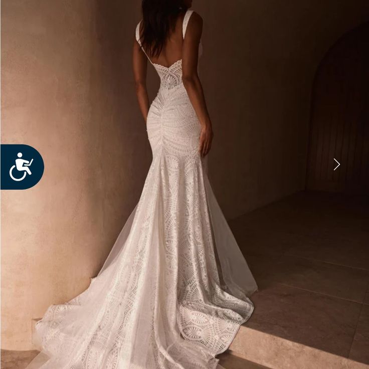 a woman in a white wedding dress standing next to a wall with her back turned towards the camera