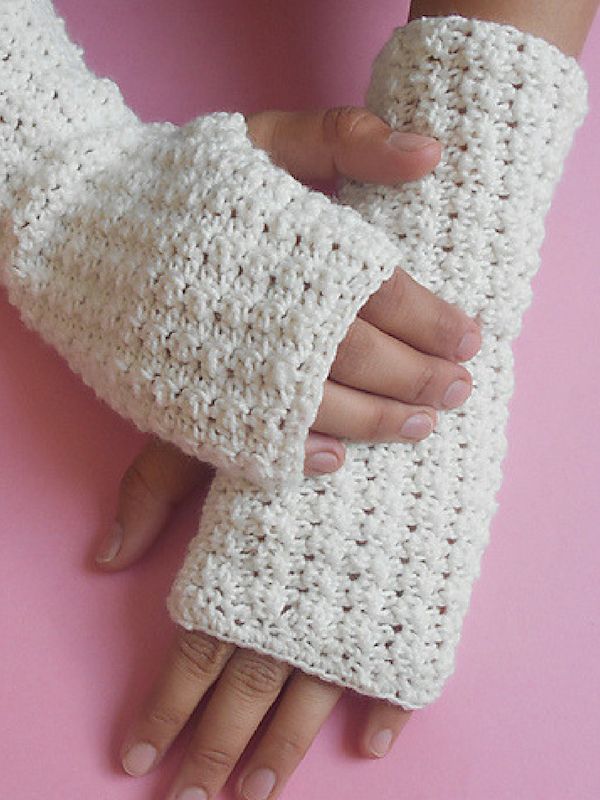 a woman's hand wearing white crocheted fingerless gloves on top of a pink surface