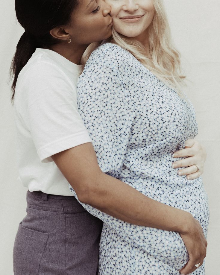 two women embracing each other while one woman is holding her pregnant baby bump up to her belly