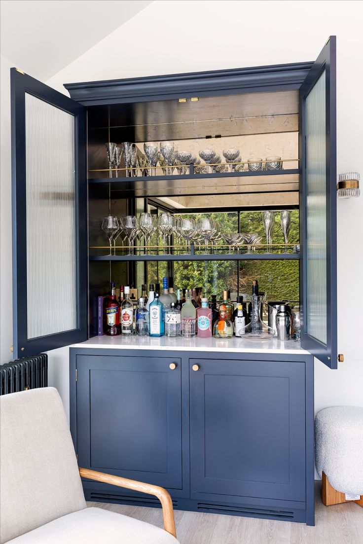 a blue cabinet filled with bottles and glasses on top of a counter next to a chair