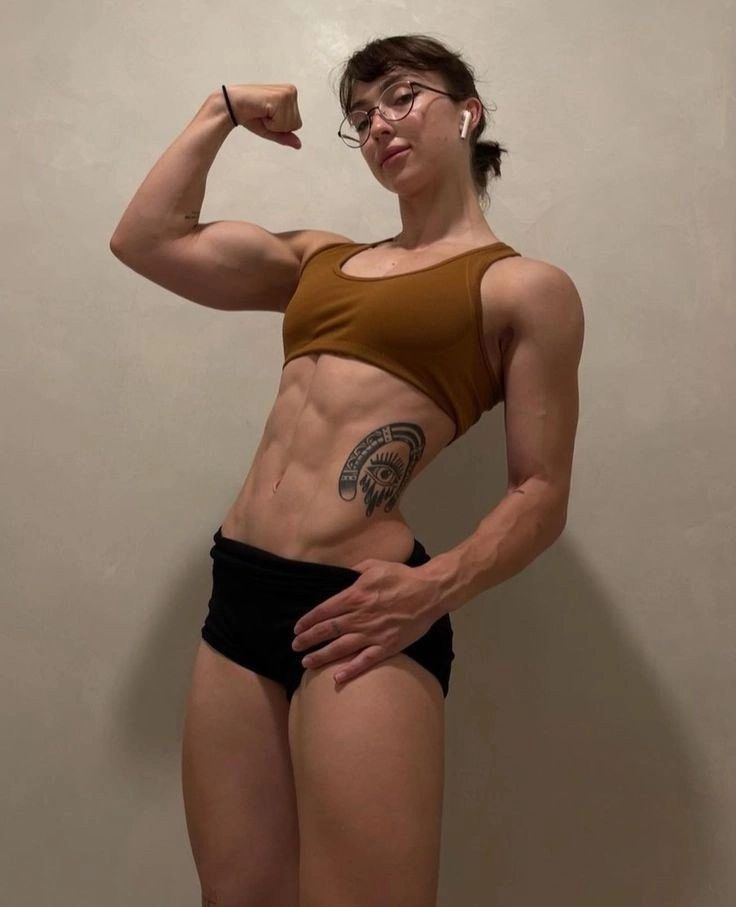 a woman posing for the camera with her arm raised and showing off her muscular body