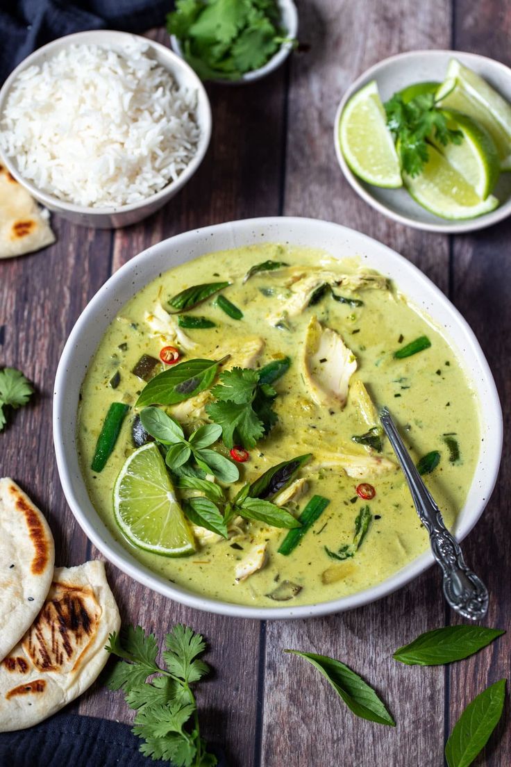 a white bowl filled with green curry next to pita bread and lime wedges