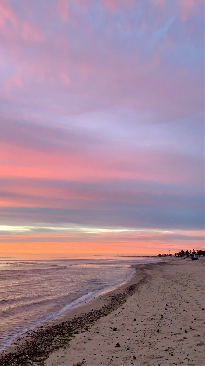 the sky is pink and purple as the sun sets on the beach with footprints in the sand