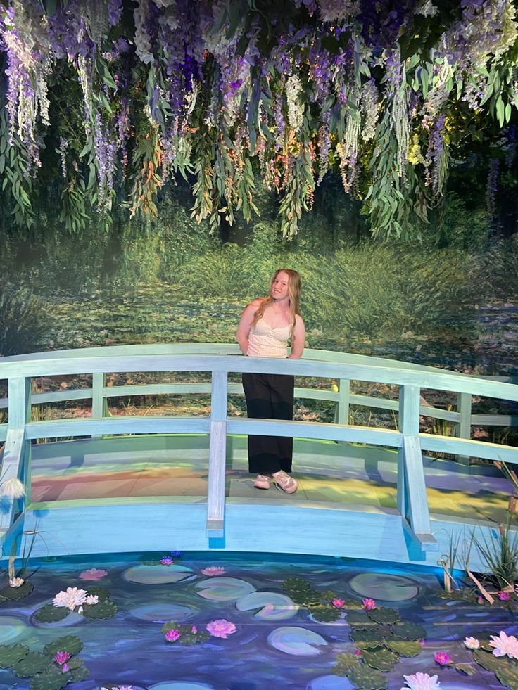 a woman standing on top of a bridge next to a pond filled with water lilies