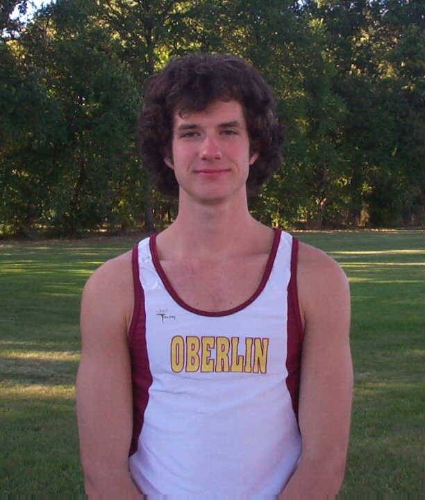 a young man standing in the grass wearing a white and maroon tank top that says obeelin