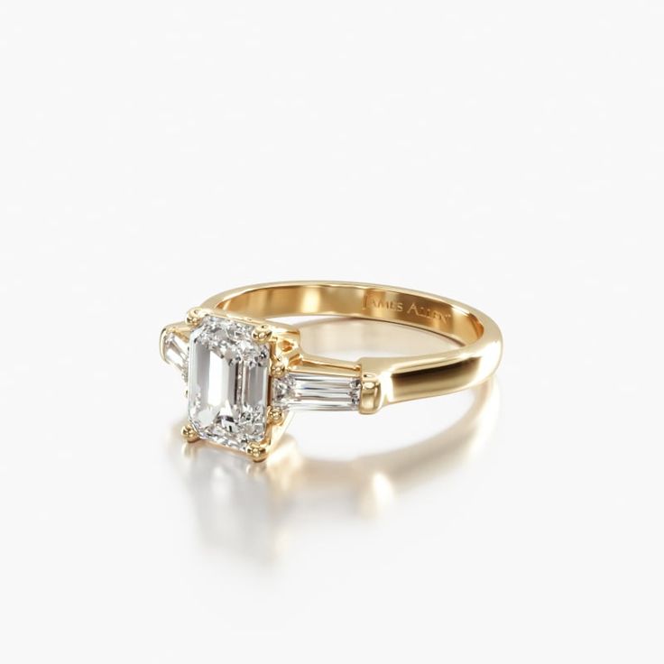 an emerald and diamond ring with two baguets in yellow gold, on a white background