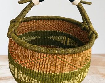 a woven basket with two handles on top of a wooden table next to a white wall