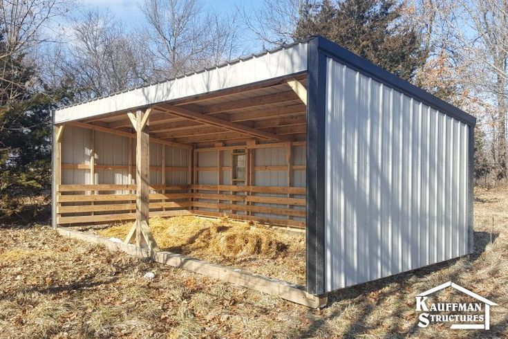 a building made out of metal and wood in the middle of a field with hay