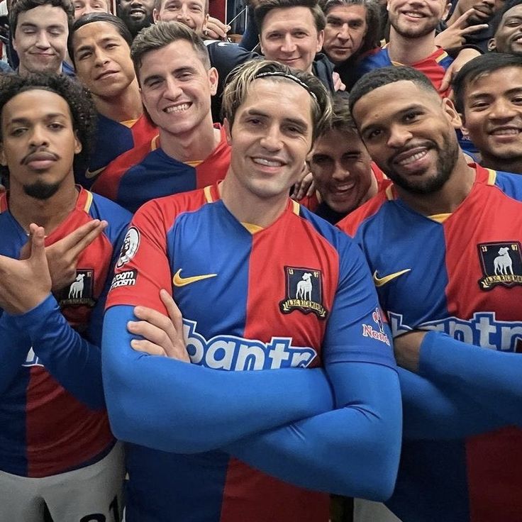 a group of men standing next to each other in front of a crowd wearing blue and red uniforms