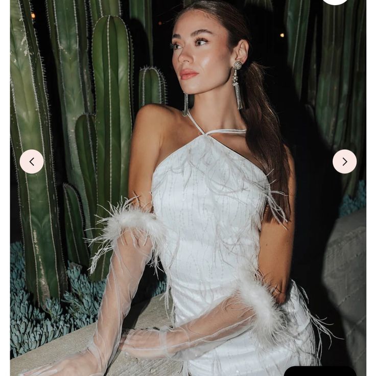 a woman in a white dress sitting next to a cactus with her hands on her hips