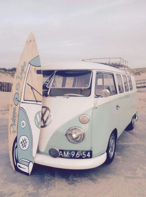 an old vw bus parked on the beach with a surfboard