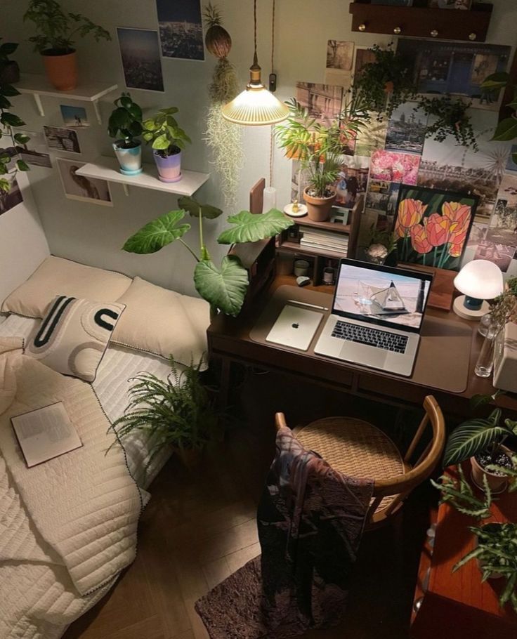 a desk with a laptop computer on top of it in a room filled with potted plants