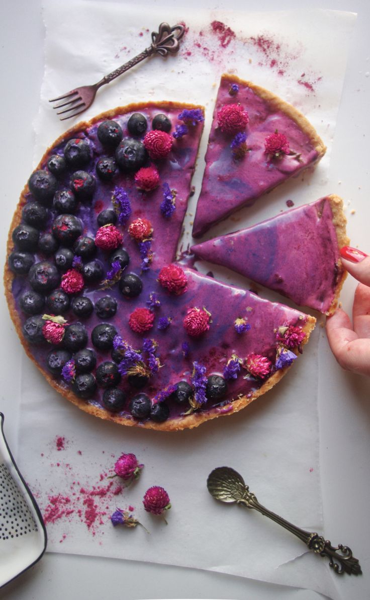 a pie with blueberries and raspberries on it is cut in half to be eaten