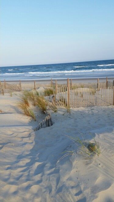 a sandy beach next to the ocean with wooden fence and grass in the foreground