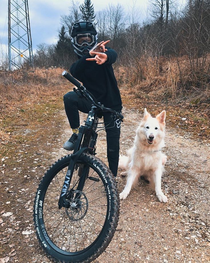 a person on a bike with a dog sitting next to it and the man is making a peace sign