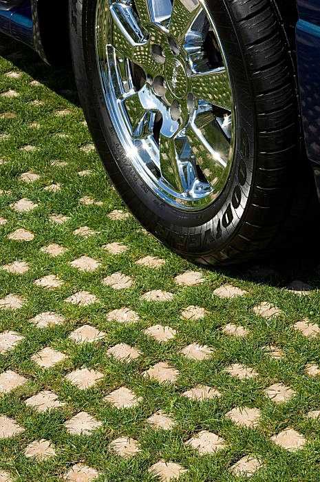 the front tire of a blue car parked on green grass with cobblestone pavement