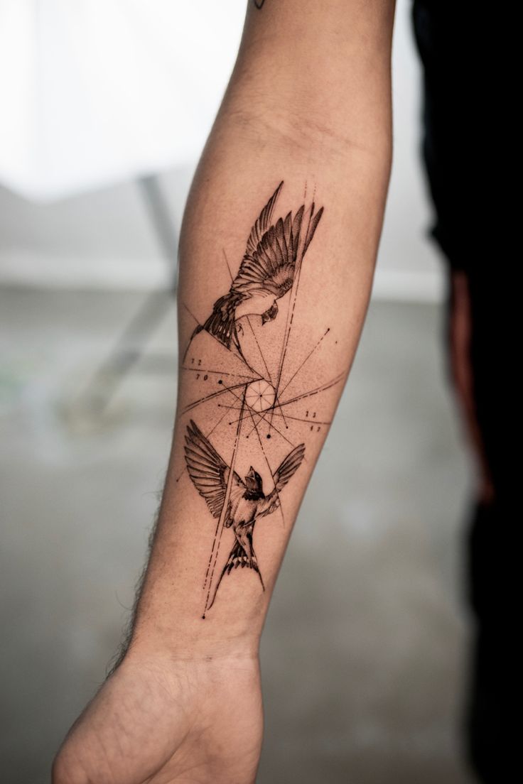 a tattoo on the arm of a man with two birds flying over it and an arrow