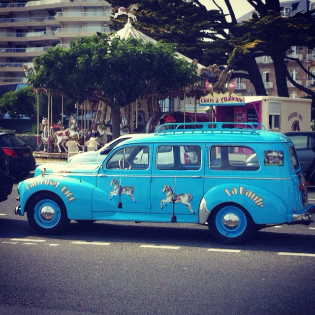 an old blue car with horses painted on it's side driving down the street