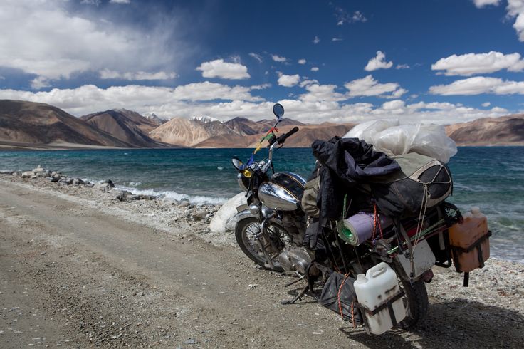 a motorcycle parked on the side of a dirt road next to a body of water