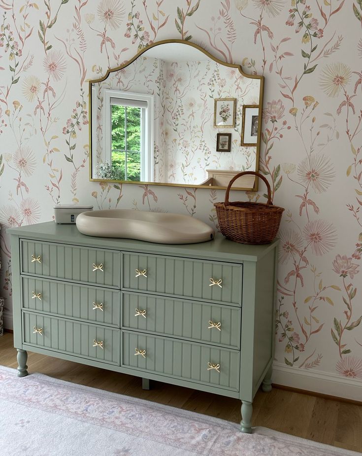 a dresser and mirror in a room with floral wallpaper on the walls behind it