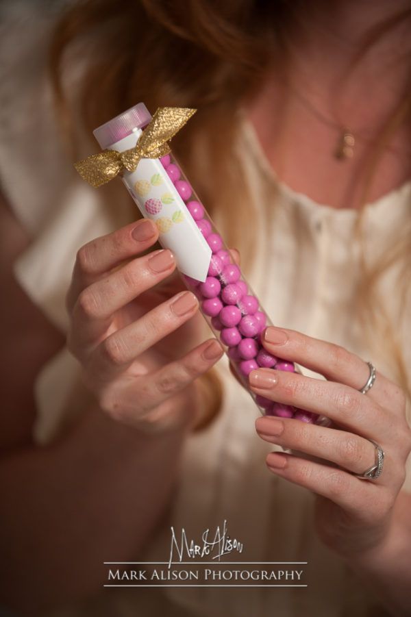 a woman holding a pink and white candy bar with gold bow on it's top