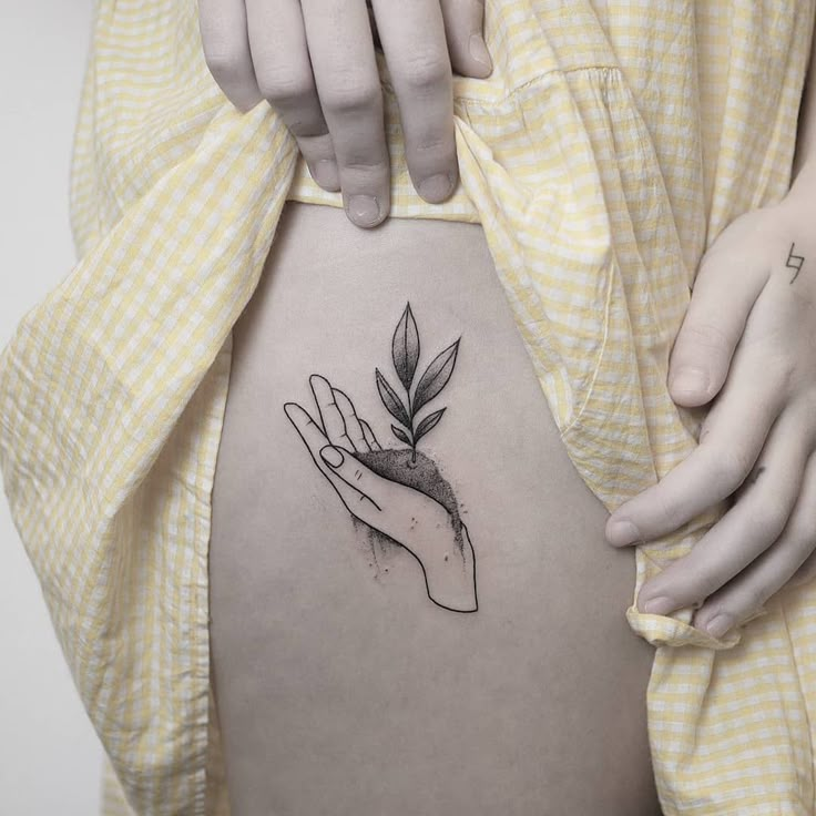 a woman's stomach with a small tattoo on the side of her belly, holding a plant