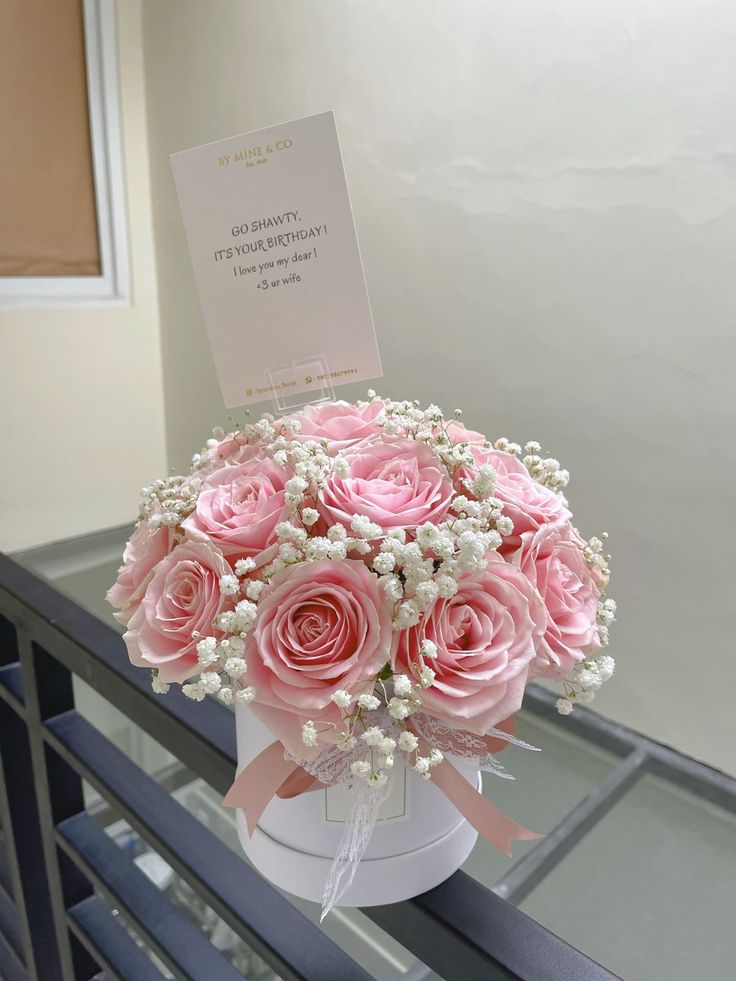 a bouquet of pink roses and baby's breath in a white vase on a railing