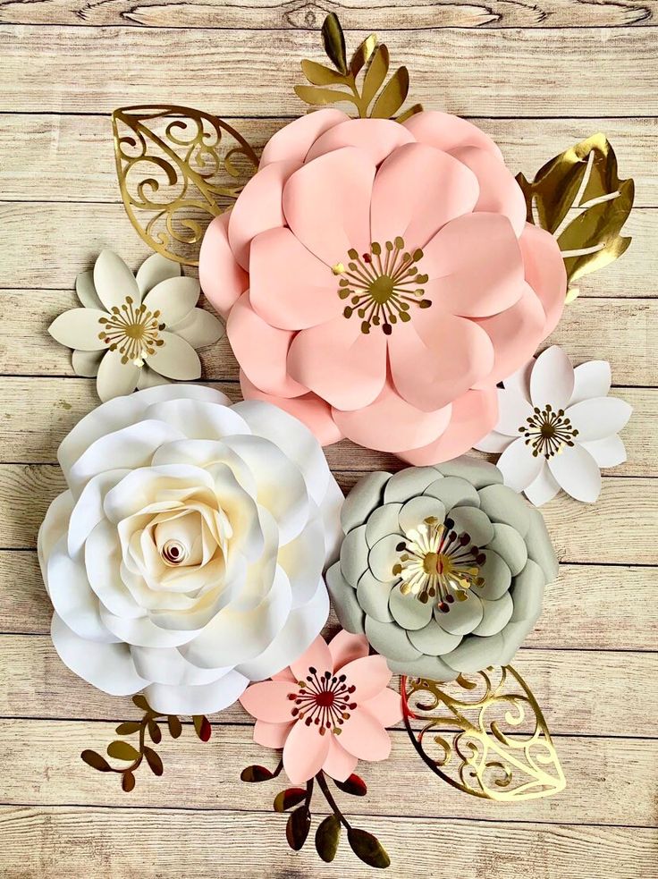 paper flowers are arranged on a wooden surface with gold foil leaves and pink, white, and gray flowers