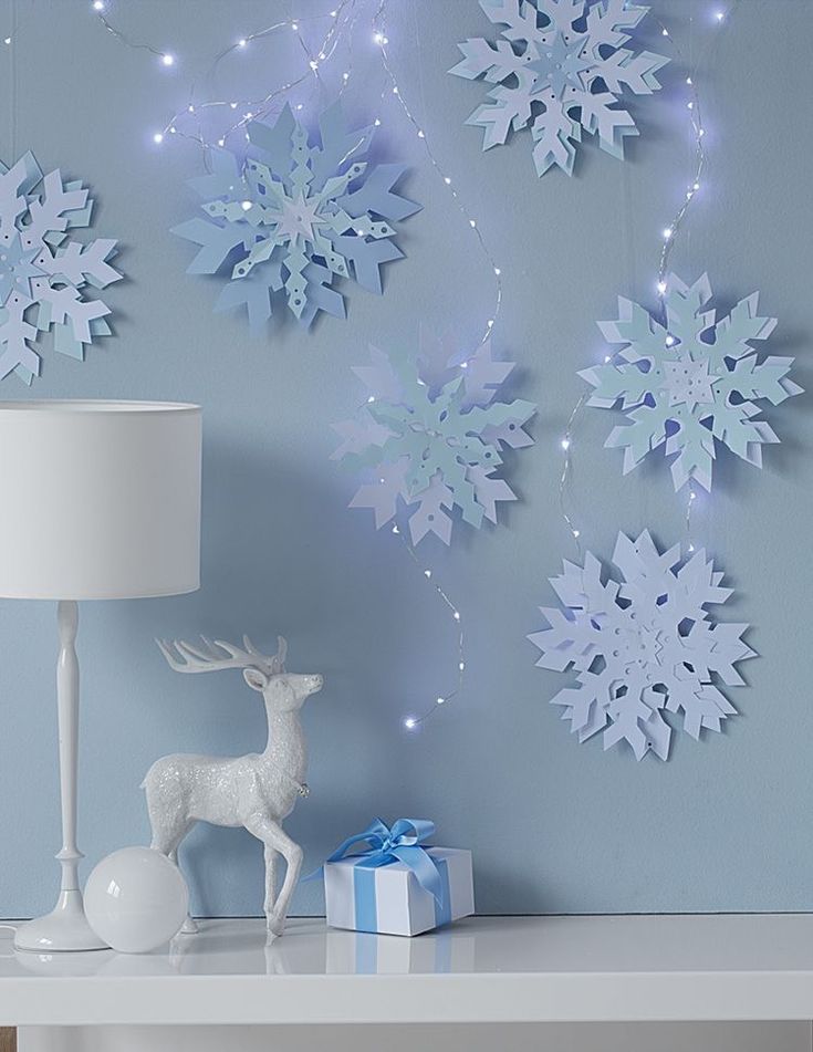 a white table topped with a lamp next to snowflakes and a deer figurine