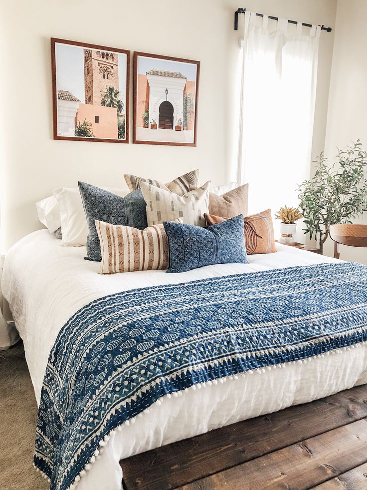 a bed with blue and white pillows on top of it next to two framed pictures