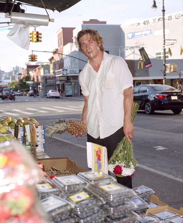 a man standing in front of a fruit stand with pineapples and other fruits