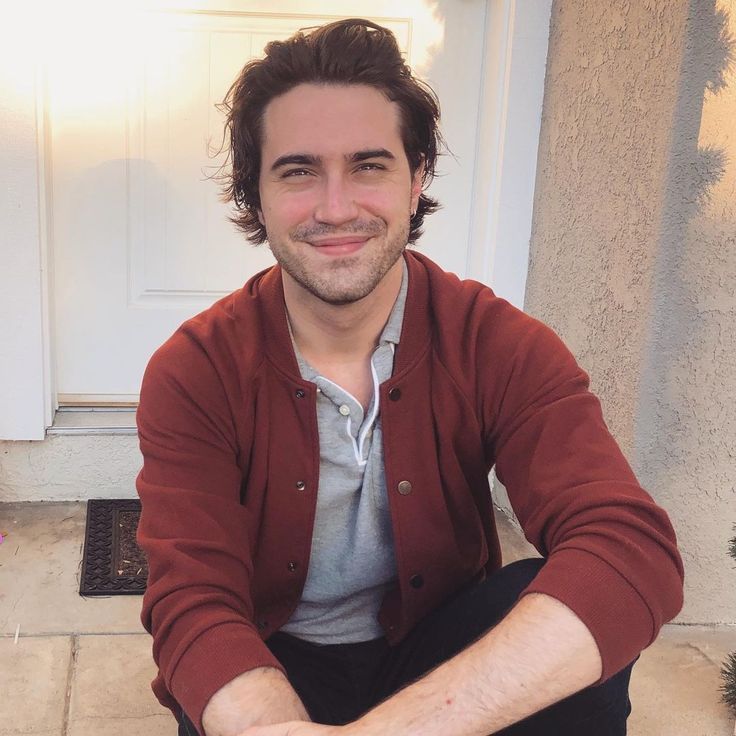 a man sitting on the ground in front of a white door smiling at the camera