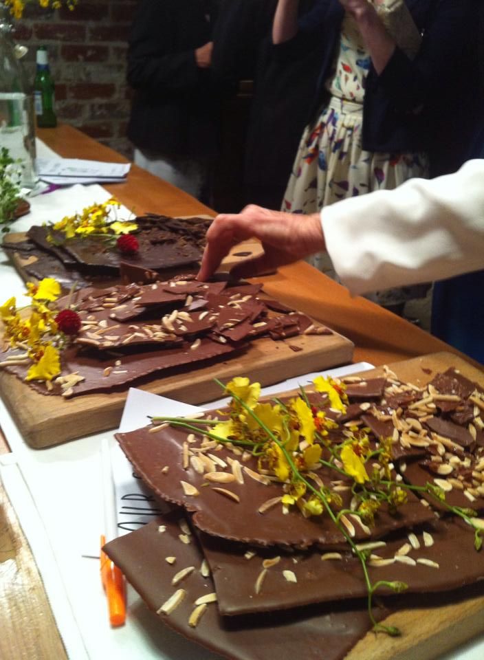 people are standing at a table with chocolate desserts on it and flowers in the middle