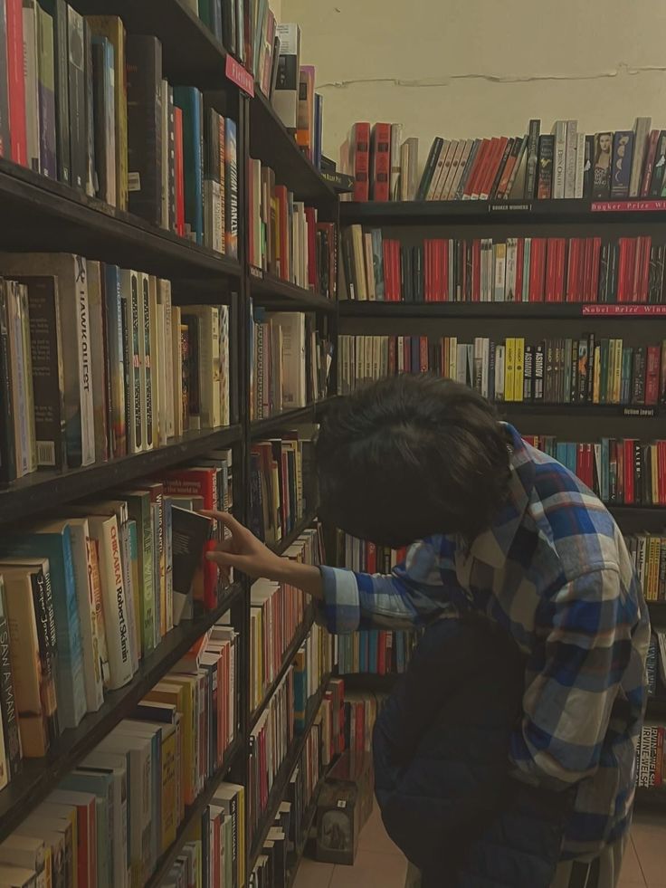 a person picking up books from a bookcase in a library with shelves full of books