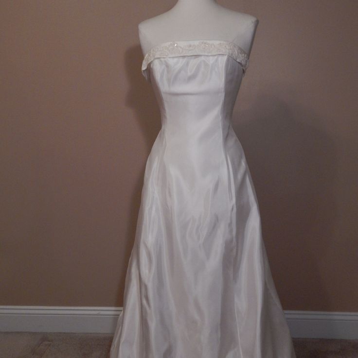 a white wedding dress on a mannequin stand in front of a brown wall