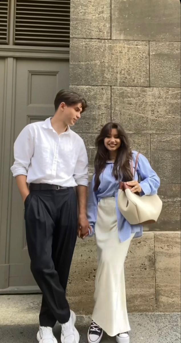 two people standing next to each other in front of a building holding hands and smiling