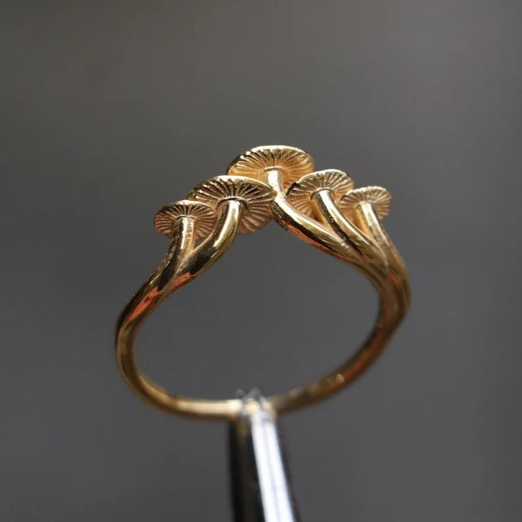 a gold ring sitting on top of a metal stand with two leaves attached to it