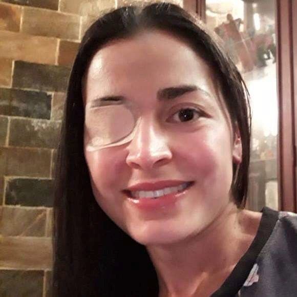 a woman with glasses smiling at the camera in front of a brick wall and door