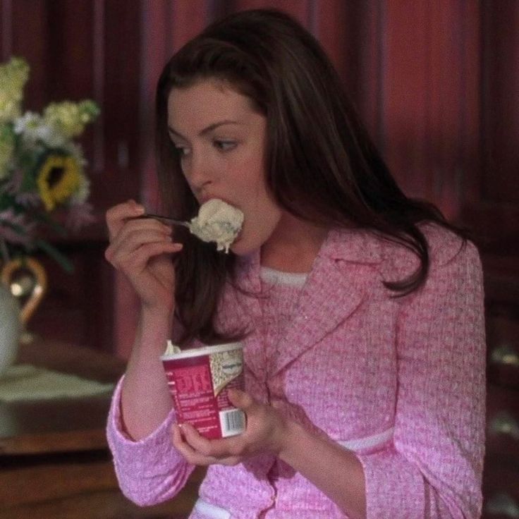 a woman in pink jacket eating food off of a cup with flowers on the side