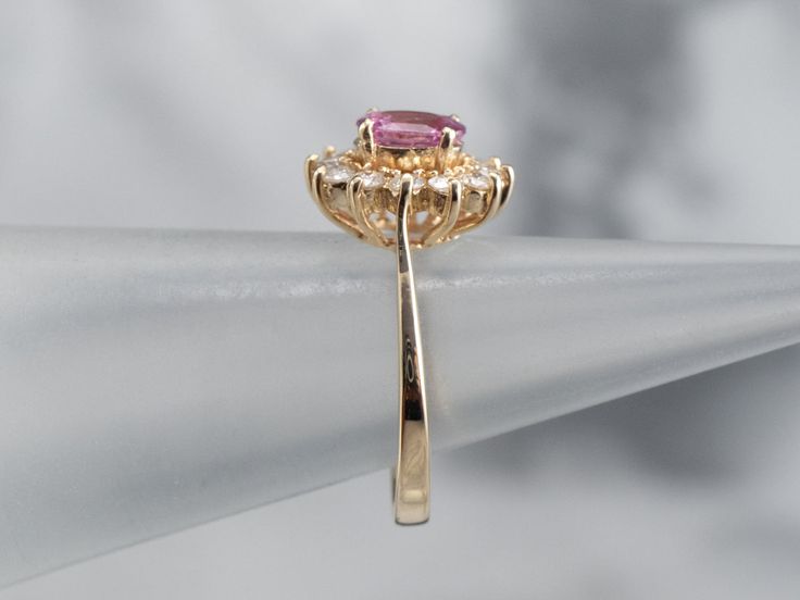 a pink diamond ring sitting on top of a white piece of paper with a gold band