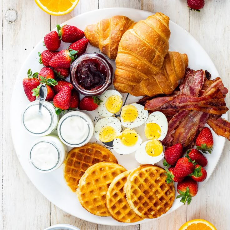 breakfast platter with bacon, eggs, croissants, strawberries and orange juice