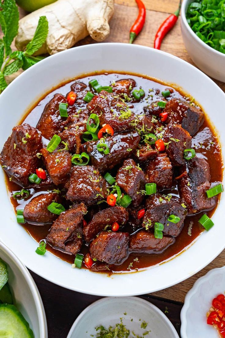 a white bowl filled with meat and vegetables on top of a wooden table next to other bowls