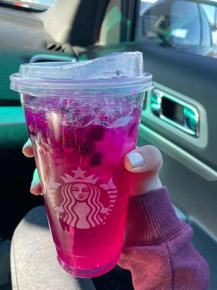 a person holding up a cup with pink liquid in it and ice on the rim