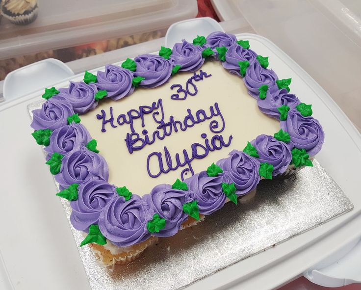 a birthday cake with purple frosting and green leaves on it sitting in a plastic container