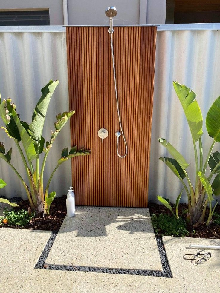 an outdoor shower is shown in front of a wooden door and some green plants on the ground