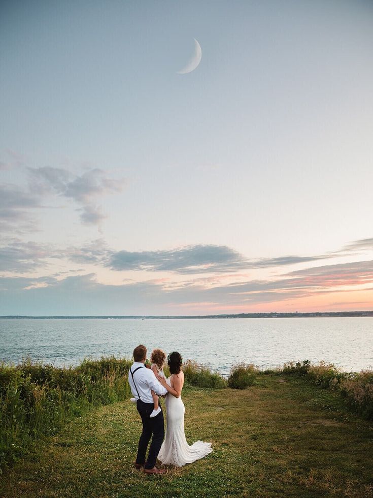 a bride and groom standing in front of the ocean at sunset