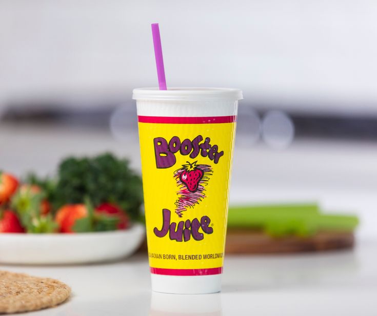 a plastic cup sitting on top of a table next to a bowl of fruit and veggies