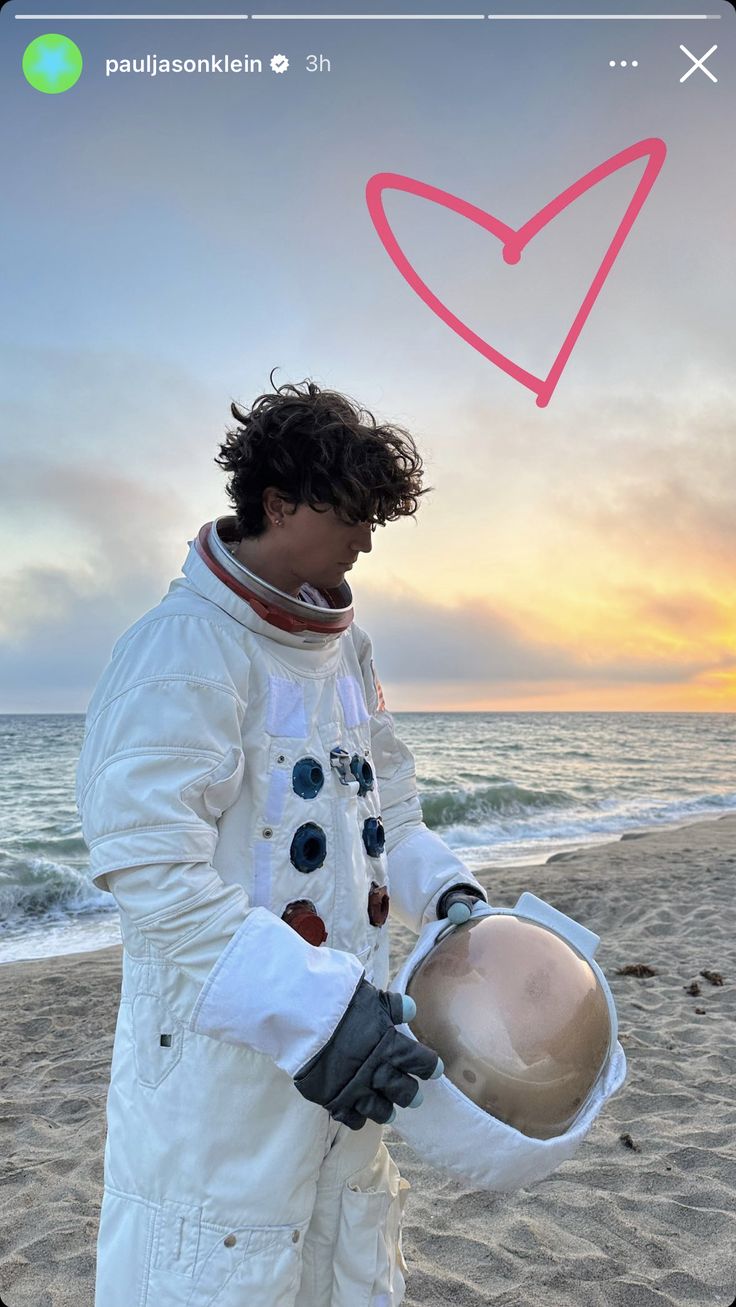 a man standing on top of a sandy beach next to the ocean wearing an astronaut suit