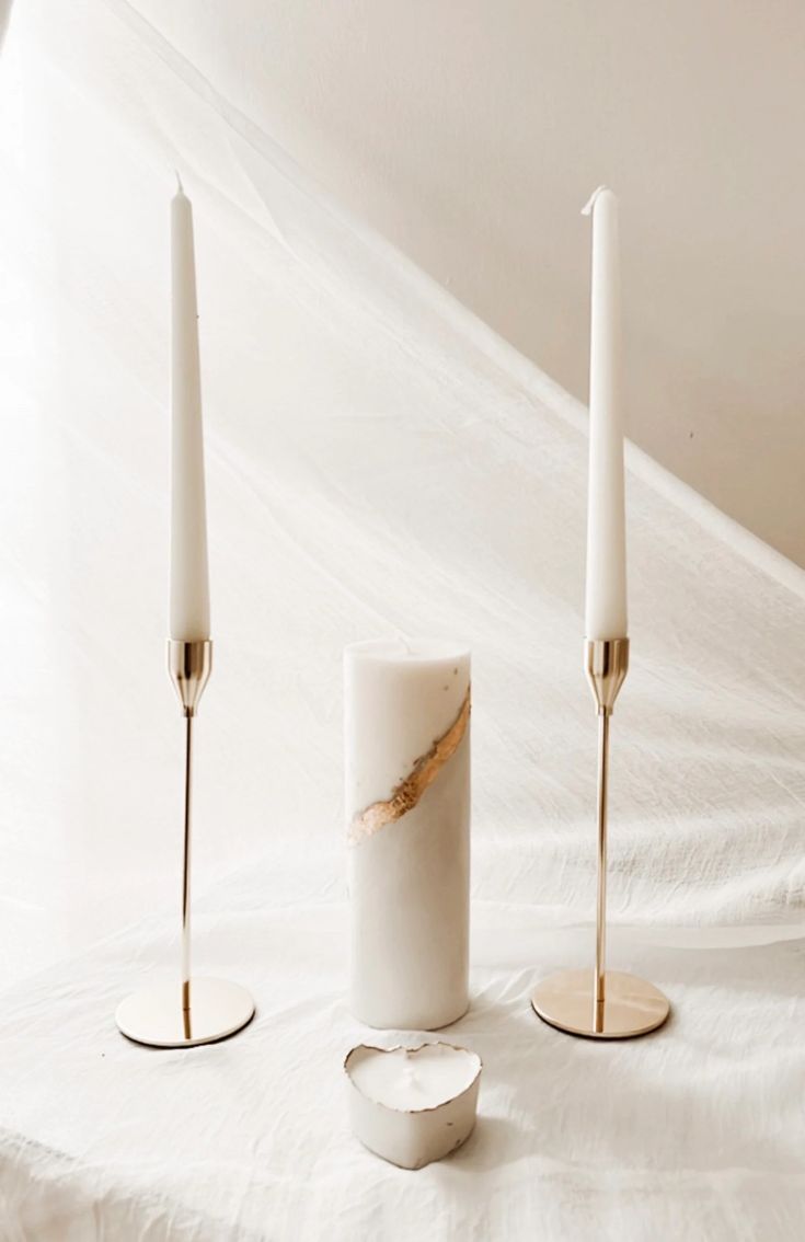 three white candles sitting on top of a bed next to each other